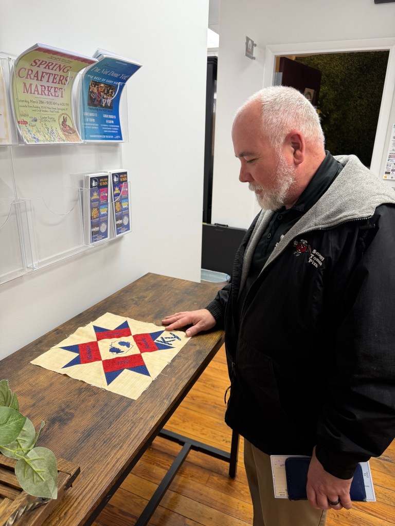 Man admires quilt square.
